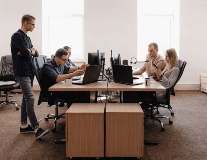 Reunião de equipe em ambiente de escritório com pessoas usando laptops e celulares para trabalho colaborativo